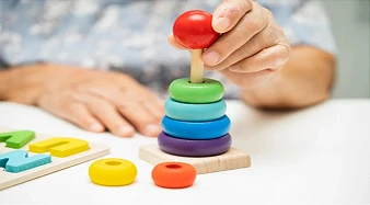 Sessão de estimulação cognitiva em Brasília. Mãos de uma especialista auxiliando um paciente em um exercício de memória e reabilitação com cartas sobre a mesa.